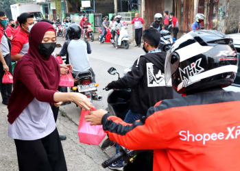 Para Ksatria dan Srikandi JNE Bogor tengah membagi-bagikan makanan kepada pengendara yang lewat dalam kegiatan Jumat Berkah