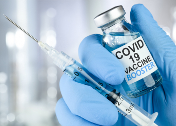 Hand in blue medical gloves holding a syringe and vaccine vial with Covid 19 Vaccine Booster text, for Coronavirus booster shot.