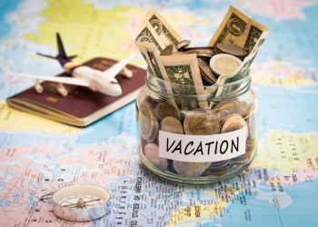 Vacation budget concept. Vacation money savings in a glass jar with compass, passport and aircraft toy on world map