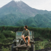 Scenic view of young Caucasian man sitting on old fashioned SUV on the background of Merapi volcano