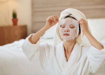 Yougn woman in bathrobe taking off moisturizing sheet mask