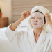 Yougn woman in bathrobe taking off moisturizing sheet mask