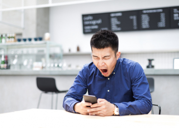 young chinese man plays with mobile phone in modern cafe. He feels tired after long-time working