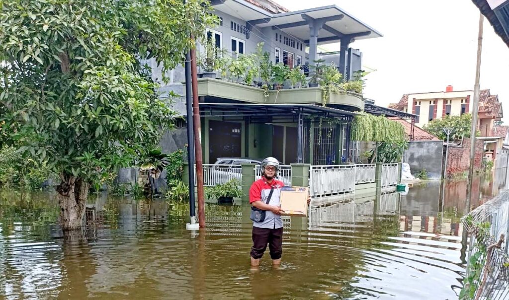 kurir jne tetap mengantar paket di tengah banjir semarang